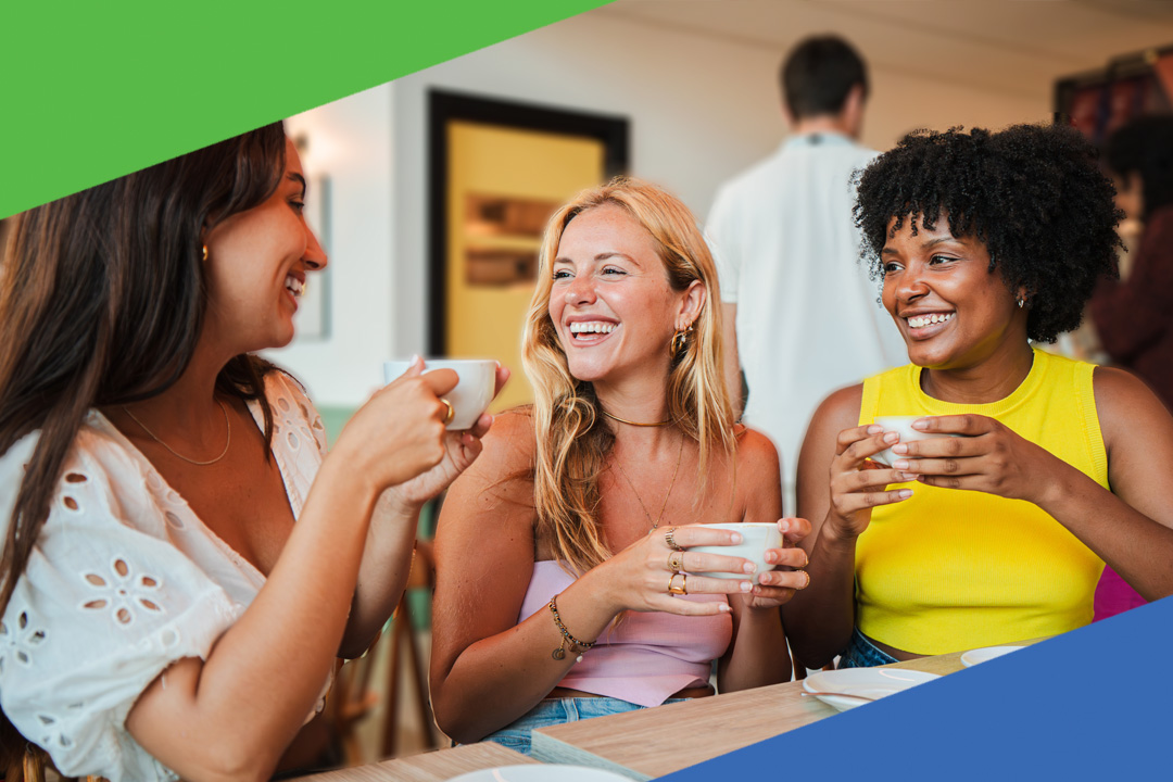 Three friends sitting at a table laughing and drinking coffee together