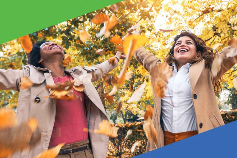 Two friends celebrating throwing autumn leaves in the air under golden trees during sunset