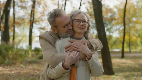 Caucasian married couple embracing together in autumn park senior man hugging from behind mature wife lovely hugs