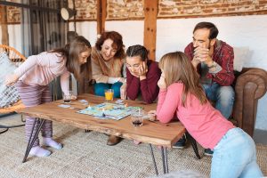 Family with children gathered around a wooden coffee table playing a board game that teaches money skills, illustrating financial education for all ages in a cozy living room.