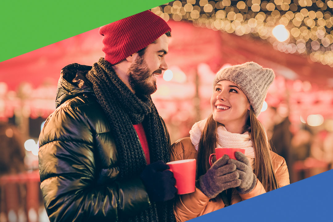Smiling couple enjoying hot drinks at a festive outdoor winter market, representing the warmth and benefits of Peake Federal Credit Union membership.