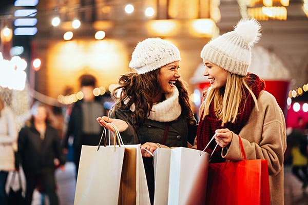 Two women enjoying holiday shopping with multiple bags, representing the rewards and convenience of the Peake Visa Platinum Card.