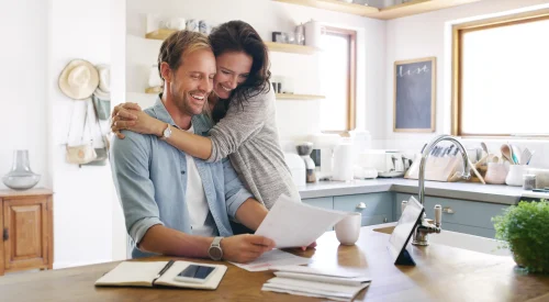 Happy, couple and hug with documents at house for financial planning, bank balance or debt payment