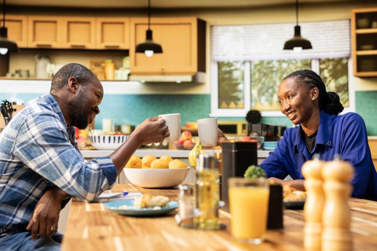 Smiling couple talking at their kitchen table over coffee, illustrating how to talk about finances without stress.