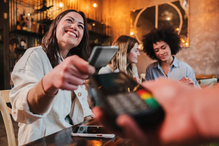Happy young woman paying bill with a contactless debit card in a restaurant