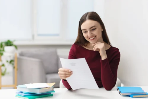 smiling woman with acceptance letter from university at table indoors