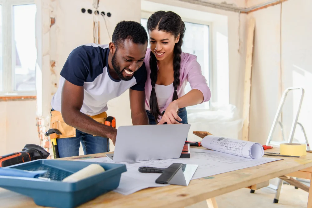 Young african american woman pointing at laptop screen to boyfriend during renovation of home