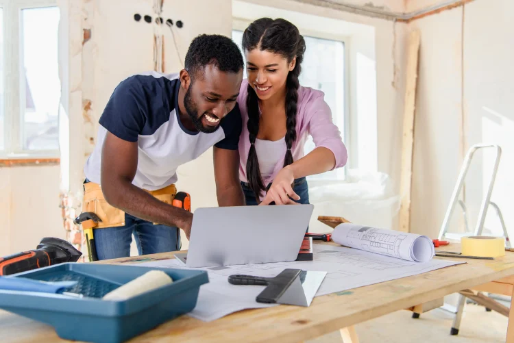 Young african american woman pointing at laptop screen to boyfriend during renovation of home